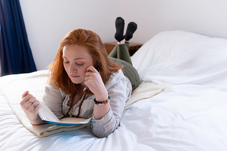 simsearch:614-01869618,k - Young woman with red hair lying on bed reading her diary Photographie de stock - Premium Libres de Droits, Code: 614-09276991