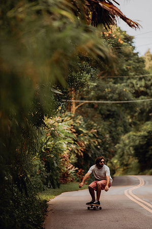 summer newest images - Mid adult male skateboarder crouching while skateboarding along rural road, Haiku, Hawaii, USA Stock Photo - Premium Royalty-Free, Code: 614-09270196