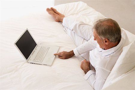Man using laptop on bed Stock Photo - Premium Royalty-Free, Code: 614-00601357