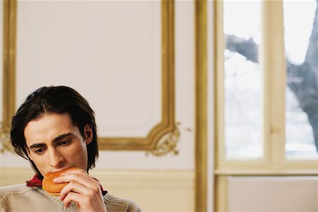 Man eating a cheeseburger and thinking Stock Photo - Premium Royalty-Free, Code: 614-00602977