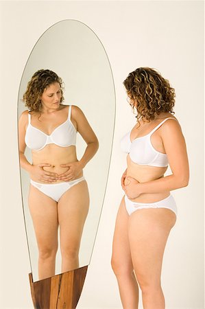 Woman looking at stomach in the mirror Stock Photo - Premium Royalty-Free, Code: 614-00892447