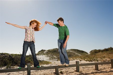 A young man helping a woman balancing on a fence Stock Photo - Premium Royalty-Free, Code: 614-02049727