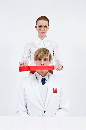 A woman covering a mans mouth with red tape Stock Photo - Premium Royalty-Free, Code: 614-02242407