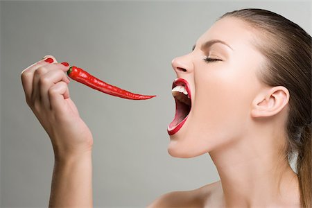 Woman biting a red chili pepper Stock Photo - Premium Royalty-Free, Code: 614-02740353