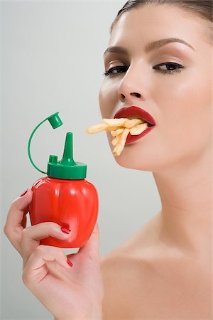 eating fries - Woman holding tomato ketchup and eating fries Stock Photo - Premium Royalty-Free, Code: 614-02740423