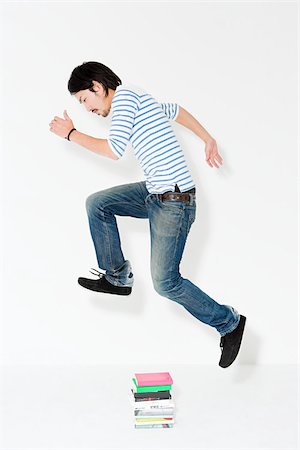Young man jumping over books Stock Photo - Premium Royalty-Free, Code: 614-02935204
