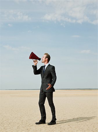 Businessman using a megaphone in the desert Stock Photo - Premium Royalty-Free, Code: 614-02984472