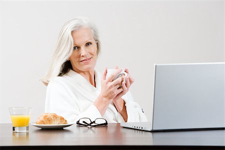 Middle aged woman eating breakfast while using laptop Stock Photo - Premium Royalty-Free, Code: 614-02983695