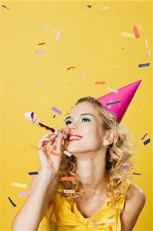 Young woman wearing party hat with party blower and confetti Stock Photo - Premium Royalty-Free, Code: 614-03507572