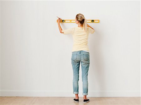 Young woman using spirit level on wall Stock Photo - Premium Royalty-Free, Code: 614-03648181