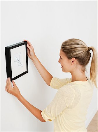 picture frames wall - Young woman hanging picture on wall Stock Photo - Premium Royalty-Free, Code: 614-03648198