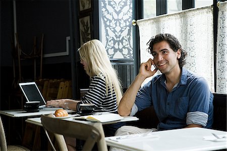 Man with cellphone and woman with laptop in cafe Stock Photo - Premium Royalty-Free, Code: 614-03649607