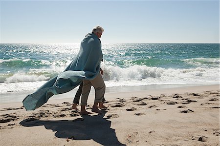 Couple d'âge mûr marchant sur la plage, enveloppée dans une couverture Photographie de stock - Premium Libres de Droits, Code: 614-03697092