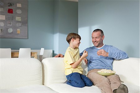 family on sofa popcorn - Father and son watching television eating popcorn Stock Photo - Premium Royalty-Free, Code: 614-03784094