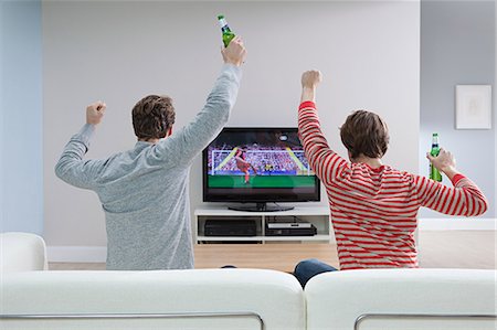 sitting on backside sofa - Two young men watching football on television Stock Photo - Premium Royalty-Free, Code: 614-03784117