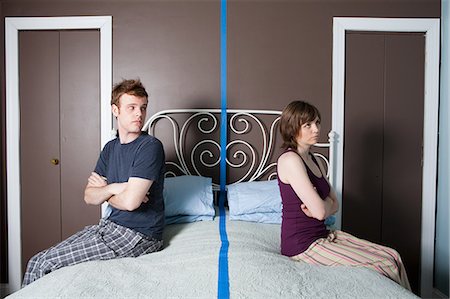 Jeune couple assis sur le lit séparé par une ligne bleue Photographie de stock - Premium Libres de Droits, Code: 614-03981511