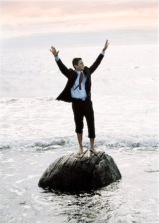 simsearch:6102-03826817,k - Un homme d'affaires debout sur une pierre dans la mer avec ses bras levés. Photographie de stock - Premium Libres de Droits, Code: 6102-03748356