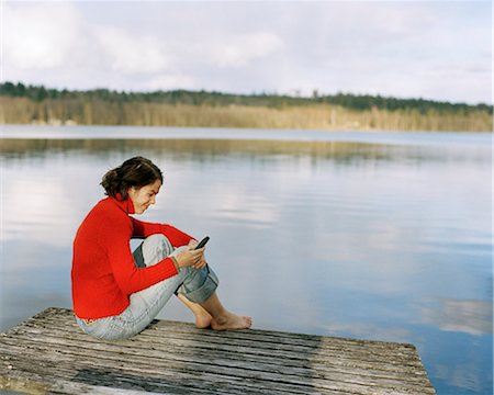 A woman with a mobile phone sitting on a bridge. Stock Photo - Premium Royalty-Free, Code: 6102-03748487