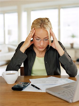 A woman concentrating in front of a pile of paper and a laptop. Stock Photo - Premium Royalty-Free, Code: 6102-03748584