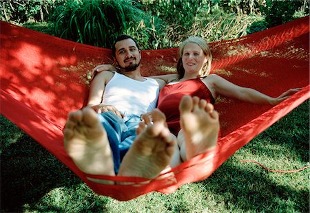 A young couple sitting in a red  hammock. Stock Photo - Premium Royalty-Free, Code: 6102-03750420