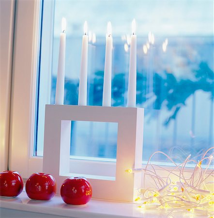 Artificial red apples with row of lighted candle on window sill at Christmas Foto de stock - Royalty Free Premium, Número: 6102-03859205