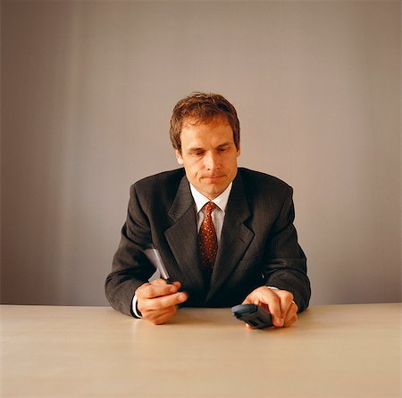 simsearch:632-06118531,k - Annoyed businessman sitting at desk holding mobile phone Stock Photo - Premium Royalty-Free, Code: 6102-03859216