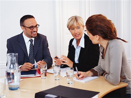 Businessman and women sitting at desk having discussion, smiling Foto de stock - Sin royalties Premium, Código: 6102-03859231