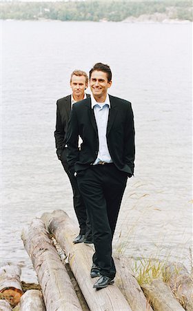 simsearch:6102-03859327,k - Two businessmen standing on logs beside sea with hands in pockets, smiling Stock Photo - Premium Royalty-Free, Code: 6102-03859329