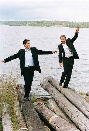 simsearch:6102-03859327,k - Two businessmen balancing on logs beside sea with arms out, smiling Stock Photo - Premium Royalty-Free, Code: 6102-03859330