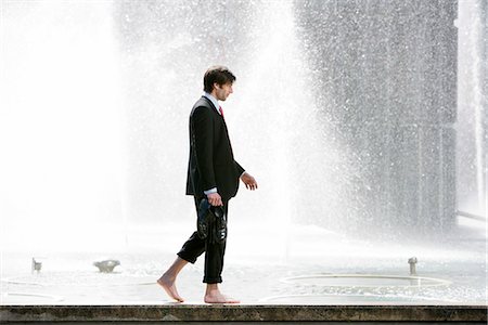 A businessman walking on a wall next to a fountain, Stockholm, Sweden. Stock Photo - Premium Royalty-Free, Code: 6102-03865709