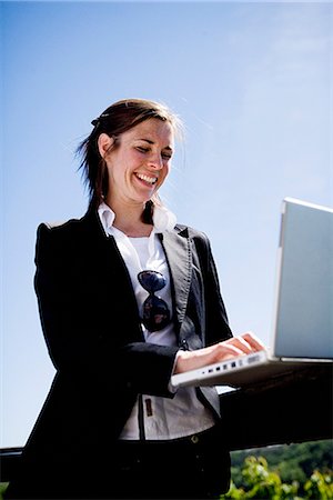 simsearch:6102-03904918,k - A smiling woman using a laptop outdoors, Sweden. Foto de stock - Royalty Free Premium, Número: 6102-03865738