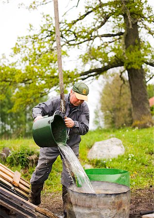 farmer with overalls - A farmer is pouring water from a bucket, Sweden. Stock Photo - Premium Royalty-Free, Code: 6102-03866088