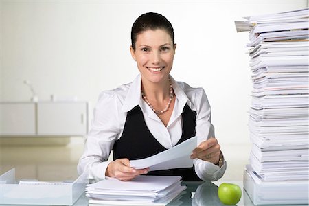 stressful women at the office with piles of work - A smiling woman doing paperwork. Stock Photo - Premium Royalty-Free, Code: 6102-03827261