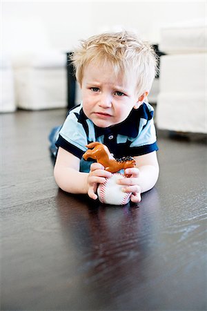 Boy lying on the floor holding toys looking sad, Stockholm, Sweden. Stock Photo - Premium Royalty-Free, Code: 6102-03827403