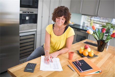 Woman sitting in kitchen doing paperwork, smiling Stock Photo - Premium Royalty-Free, Code: 6102-04929449