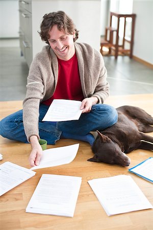 simsearch:6102-04929476,k - Mid-adult man arranging domestic paperwork on floor, while dog is sleeping next to him Fotografie stock - Premium Royalty-Free, Codice: 6102-04929506