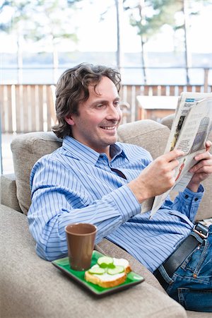 Mid-adult man sitting on sofa, reading newspaper Fotografie stock - Premium Royalty-Free, Codice: 6102-04929525