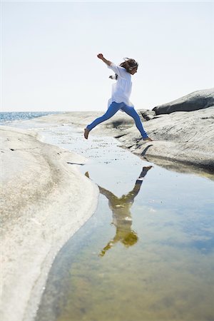 Woman jumping over water to rock Stock Photo - Premium Royalty-Free, Code: 6102-04929646