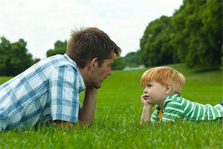 simsearch:6102-06336872,k - Père et fils se trouvant sur la pelouse dans le parc Photographie de stock - Premium Libres de Droits, Code: 6102-04929878