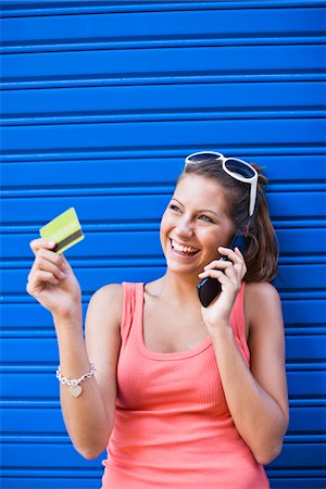 simsearch:6102-04929804,k - Young woman in front of blue wall, holding credit card and talking on phone Stock Photo - Premium Royalty-Free, Code: 6102-04929813