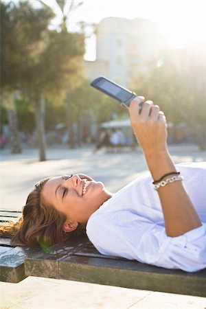 Girl lying on park bench, using cell phone Stock Photo - Premium Royalty-Free, Code: 6102-04929815