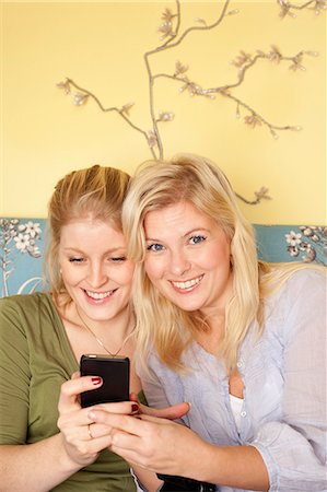 Two young women using mobile phone in bedroom Stock Photo - Premium Royalty-Free, Code: 6102-06025800