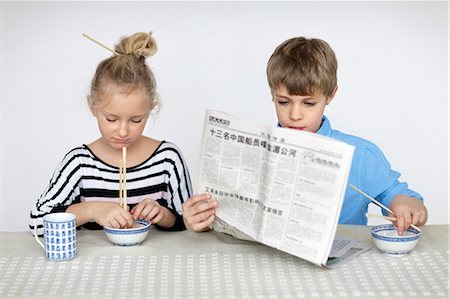 Girl eating with chopsticks and boy reading newspaper Stock Photo - Premium Royalty-Free, Code: 6102-06336639