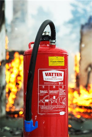 Close-up of fire extinguisher, flames in background Stock Photo - Premium Royalty-Free, Code: 6102-06337042