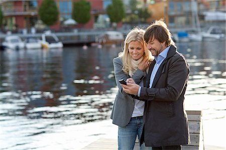 Couple standing on promenade using cell phone together Stock Photo - Premium Royalty-Free, Code: 6102-06777360