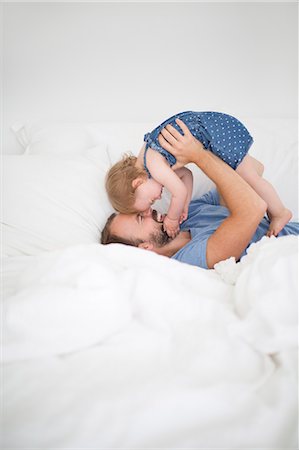 family playing bed laughing - Man lying on bed and holding little daughter Stock Photo - Premium Royalty-Free, Code: 6102-06777446