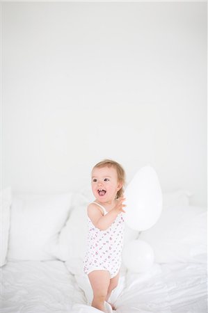 Little girl standing on bed and holding balloon Stock Photo - Premium Royalty-Free, Code: 6102-06777454