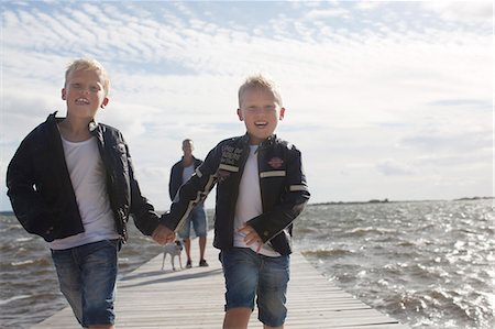 simsearch:6102-06965802,k - Two boys on jetty, father in background Fotografie stock - Premium Royalty-Free, Codice: 6102-06965573