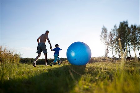 dad exercising - Man running with boy, blue ball on foreground, Norrbotten, Sweden Stock Photo - Premium Royalty-Free, Code: 6102-07768336