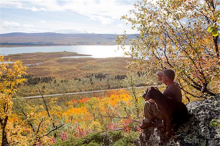 Man sitting with dog and looking at view, Kiruna, Norrbotten, Lapland, Sweden Foto de stock - Royalty Free Premium, Número: 6102-07768686